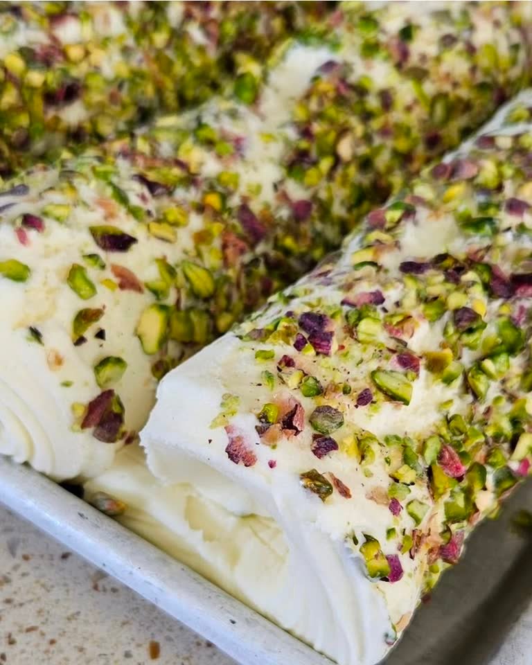A cut roll of Ashta booza, white and dense, crusted in chopped pistachios and dried rose petals.